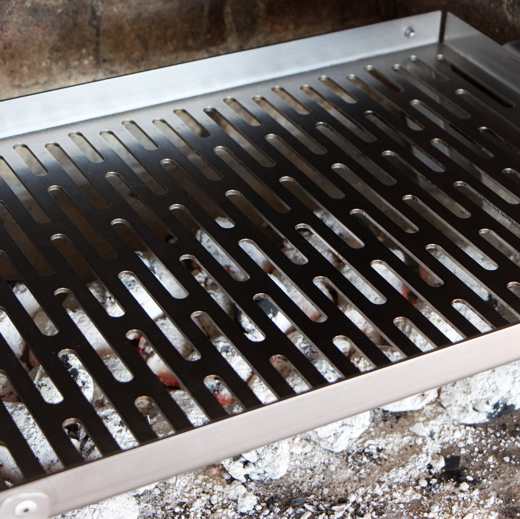 Stainless steel braai grid with visible coals underneath