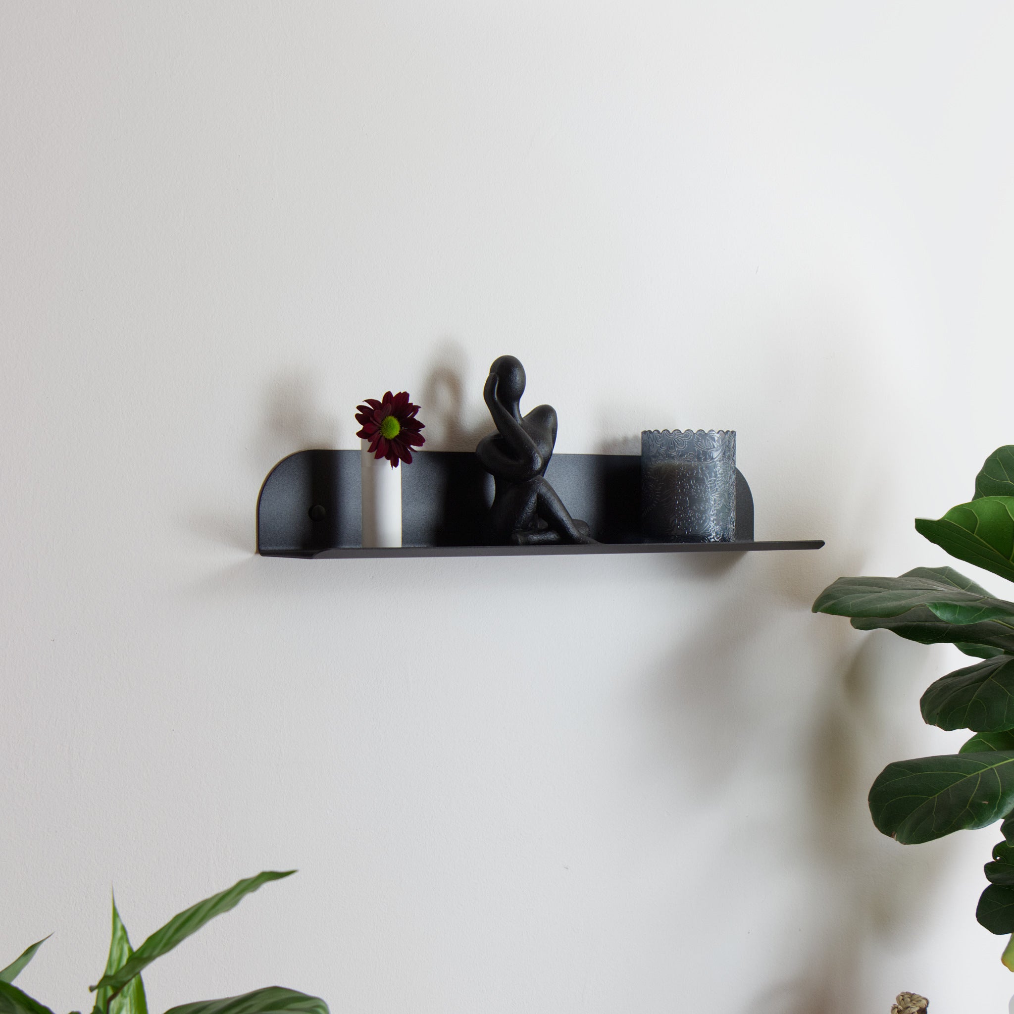 Black wall shelf with decorative items on a white wall