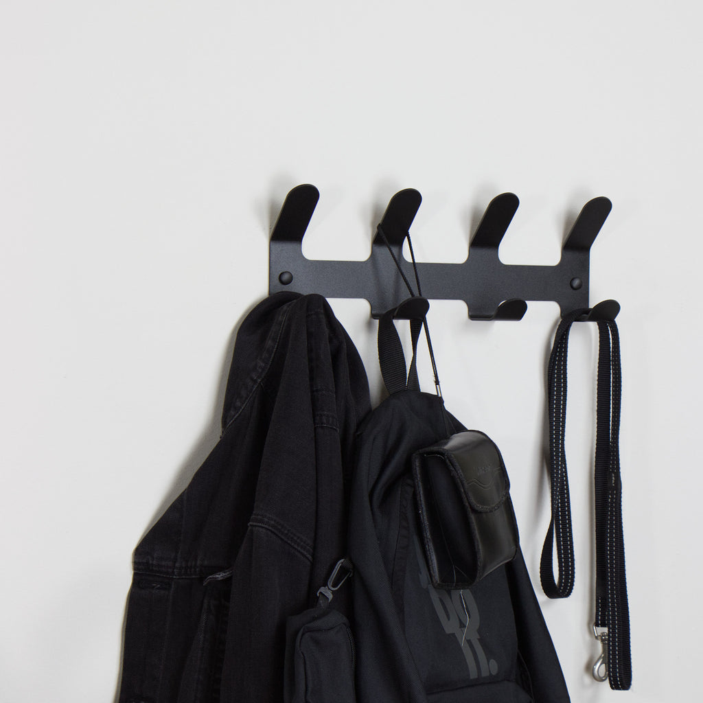 Black wall-mounted coat rack with hooks holding a jacket, bag, and leash on a white background
