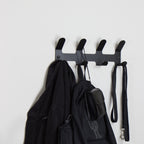 Black wall-mounted coat rack with hooks holding a jacket, bag, and leash on a white background